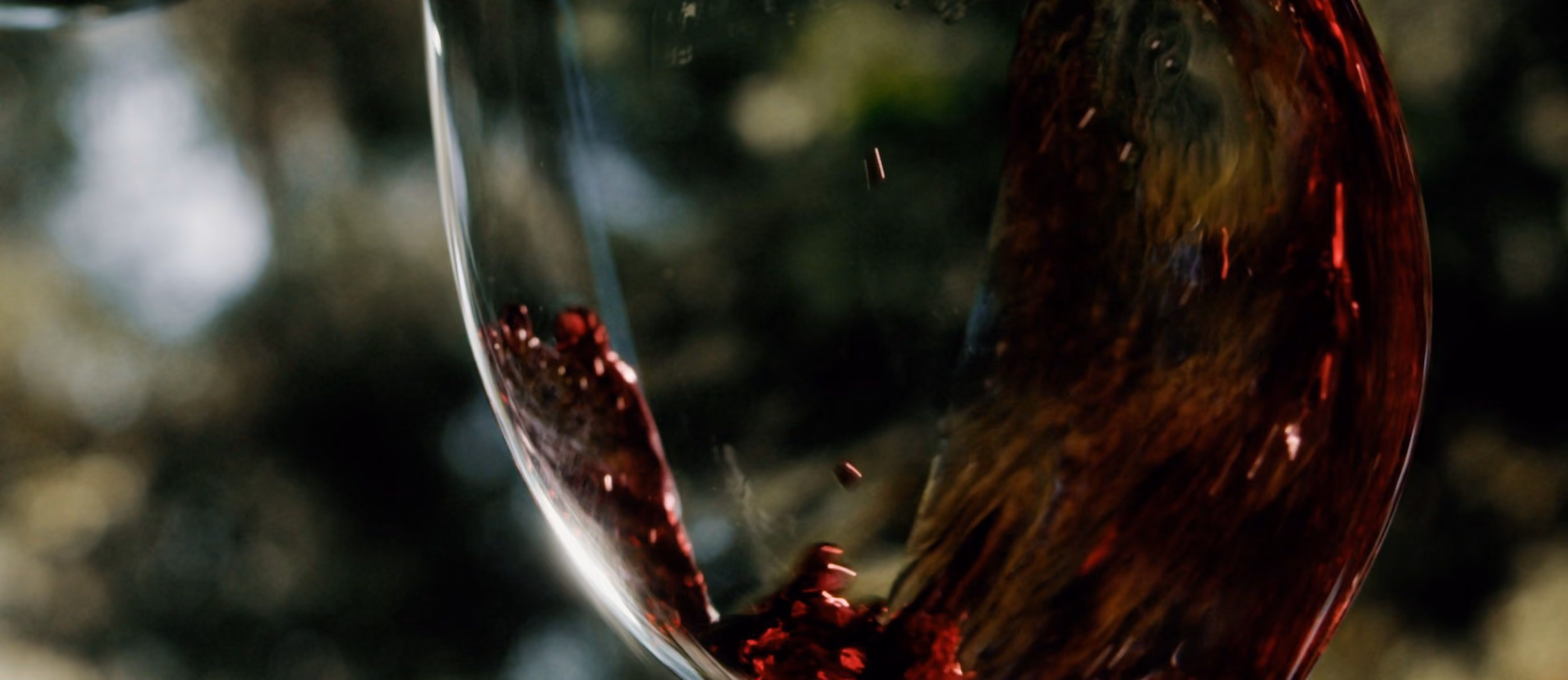 Vino tinto girando dentro de la copa sobre fondo verde oscuro